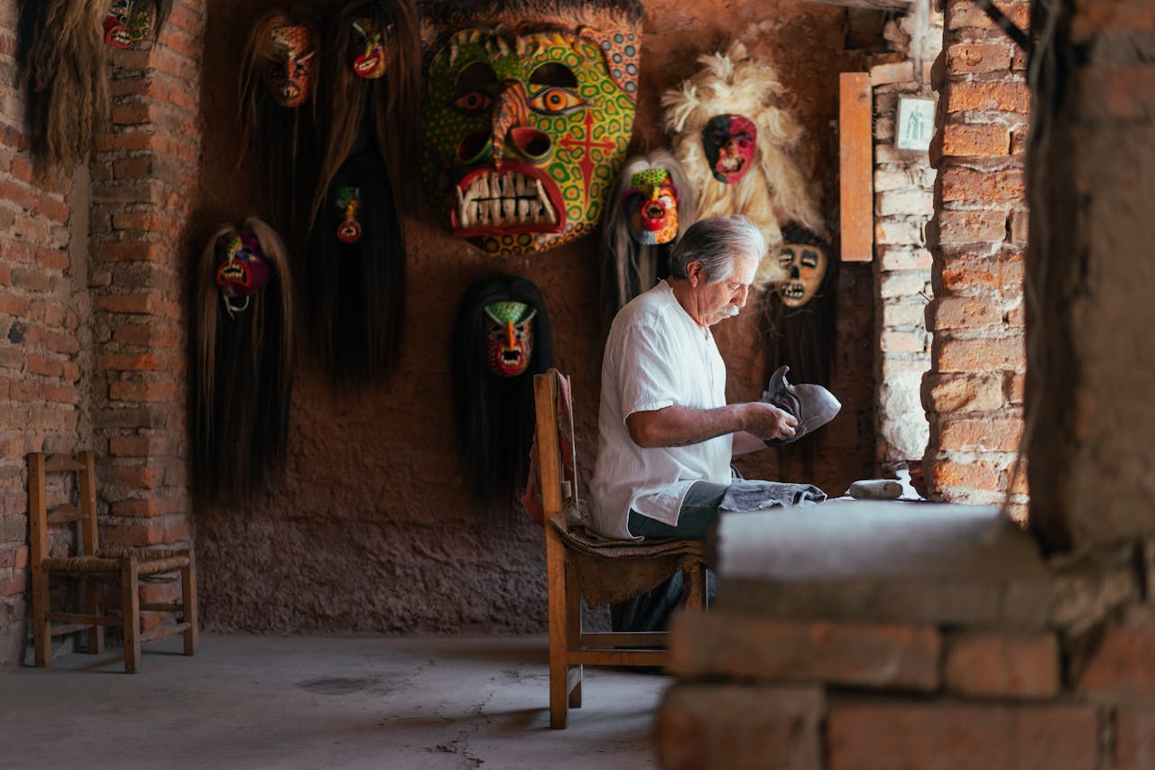 Elderly man crafting traditional Mexican masks in a rustic indoor setting.